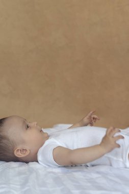 6-8 aylık erkek bebek yatakta eğlenceli bir şekilde yatıyor. Beyaz bodysuit büyüleyici 6-7 aylık küçük bebek. Beyaz yataklı bebek. Kopyalama alanı