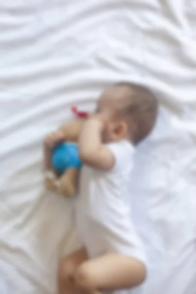 Niño de 6-8 meses acostado juguetonamente en la cama. Encantador bebé de 6-7 meses en traje de cuerpo blanco. Niño en ropa de cama blanca. Copiar espacio — Foto de Stock