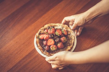 Elinde çilek ve çikolata kreması olan bir tabak ince krep tutan genç bir kadın. Taze çilek ile krep yiyen kadın