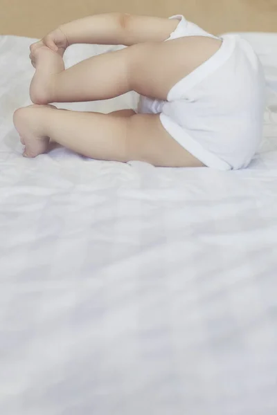 En 6-8 måneder gammel gutt som ligger lekent i senga. Sjarmerende 6-7 måneder med hvit kroppsdress. En liten gutt i hvit seng. Kopirom – stockfoto