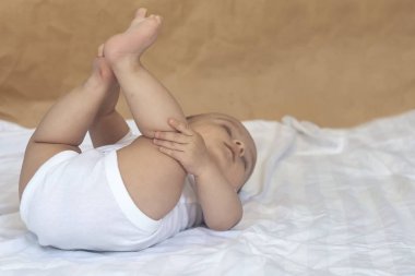 6-8 aylık erkek bebek yatakta eğlenceli bir şekilde yatıyor. Beyaz bodysuit büyüleyici 6-7 aylık küçük bebek. Beyaz yataklı bebek. Kopyalama alanı
