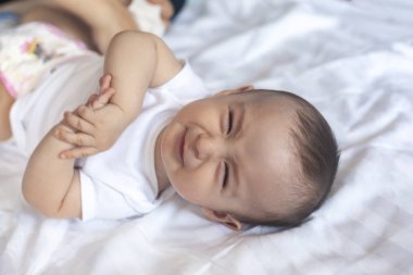 Kızgın 6 aylık bebek yatakta. Küçük bebek çocuk rahatsız ve mutsuz hissediyor. Üzgün bebek kameraya bakıyor. Kopyalama alanı