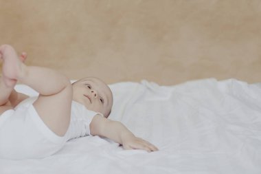 6-8 aylık erkek bebek yatakta eğlenceli bir şekilde yatıyor. Beyaz bodysuit büyüleyici 6-7 aylık küçük bebek. Beyaz yataklı bebek. Kopyalama alanı