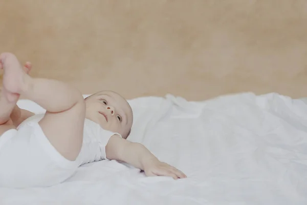 6-8 개월 된 아기 소년이 침대에 장난스럽게 누워 있습니다. 흰색 바디 수트에 매력적인 6-7 개월 작은 아기. 흰색 침구에 아기 소년입니다. 복사 공간 — 스톡 사진