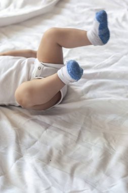 Bacaklarının 6-8-ay-yaşlı bebek beyaz bodysuit yatakta oynuyor. Boşluk Kopyala