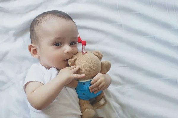 6-8-maand-oude baby jongen liggend spelvol in bed. Charmante 6-7 maand kleine baby in witte Romper. Baby jongen in wit beddengoed. Ruimte kopiëren — Stockfoto