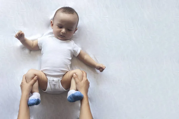 Massagem de bebé. A mãe faz ginástica com o miúdo. Mamãe massagear menino bonito. Movendo as pernas do bebê para ajudar a aliviar a constipação. Jovem mãe fazendo exercícios e movimentos para estimular os intestinos do bebê . — Fotografia de Stock