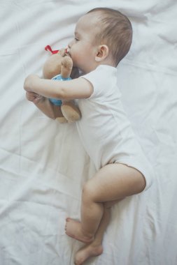 6-8 aylık erkek bebek yatakta eğlenceli bir şekilde yatıyor. Beyaz bodysuit büyüleyici 6-7 aylık küçük bebek. Beyaz yataklı bebek. Kopyalama alanı