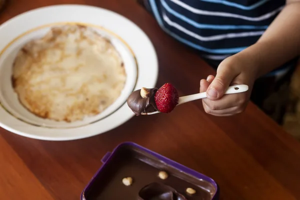 Ein kleiner Junge mit seiner Mutter, die gemeinsam ein Frühstück zubereitet. Mutter und Sohn schmieren Schokoladencreme zu dünnen Pfannkuchen. Freiraum — Stockfoto