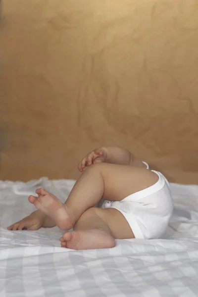 Niño de 6-8 meses acostado juguetonamente en la cama. Encantador bebé de 6-7 meses en traje de cuerpo blanco. Niño en ropa de cama blanca. Copiar espacio — Foto de Stock