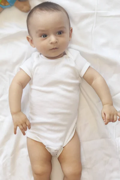 Menino de 6-8 meses deitado na cama. Encantador bebê de 6-7 meses de macacão branco. Menino de cama branca. Espaço de cópia — Fotografia de Stock