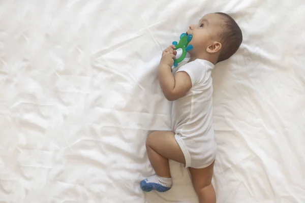 Niño de 6-8 meses acostado juguetonamente en la cama. Encantador bebé de 6-7 meses en traje de cuerpo blanco. Niño en ropa de cama blanca. Copiar espacio — Foto de Stock