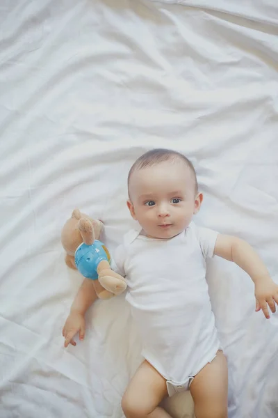 6-8-maand-oude baby jongen liggend spelvol in bed. Charmante 6-7 maand kleine baby in witte Romper. Baby jongen in wit beddengoed. Ruimte kopiëren — Stockfoto
