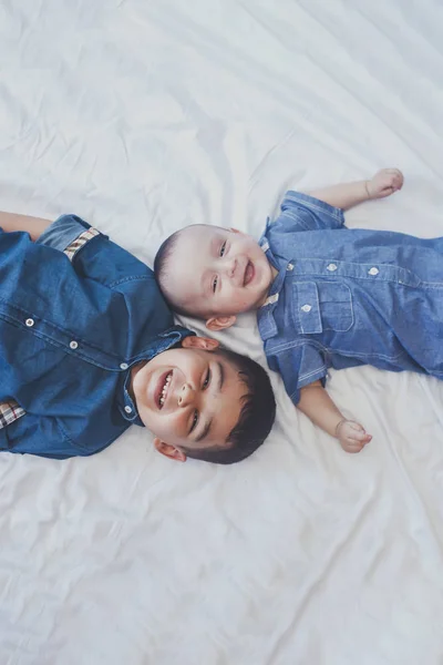 행복 한 어린 시절 개념입니다. 행복한 형제 초상화입니다. 6 년 소년과 6 개월 된 아기 소년이 재미있습니다. 두 어린 아이들이 카메라를 향해 미소짓고 있습니다. 귀여운 작은 형제 누워 에 침대 함께 — 스톡 사진