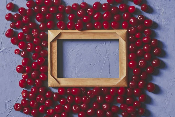 Marco de madera con espacio de copia y cerezas maduras sobre fondo azul. Bayas y frutas alrededor del marco de madera vacío — Foto de stock gratuita