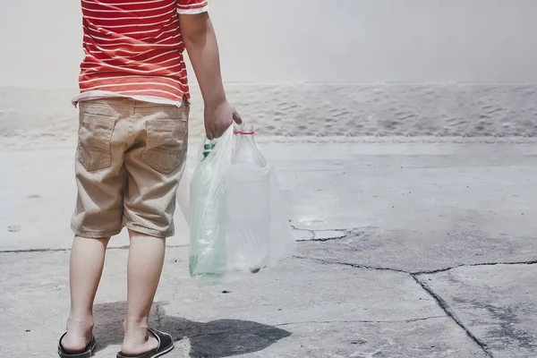 Пластиковые загрязнения на суше. Мальчик собирает пластиковые бутылки. Ребенок несет мешок для мусора. Свободное пространство — стоковое фото