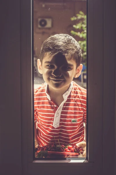 Petit garçon debout dehors avec un bol de cerises et regardant par la porte. Enfance, concept d'été — Photo