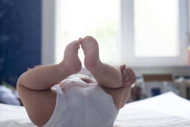 6 aylık bebek beyaz yatak içinde eğleniyor. Yatakta yatan sevimli bir bebek. Aile, yeni yaşam, çocukluk konsepti.