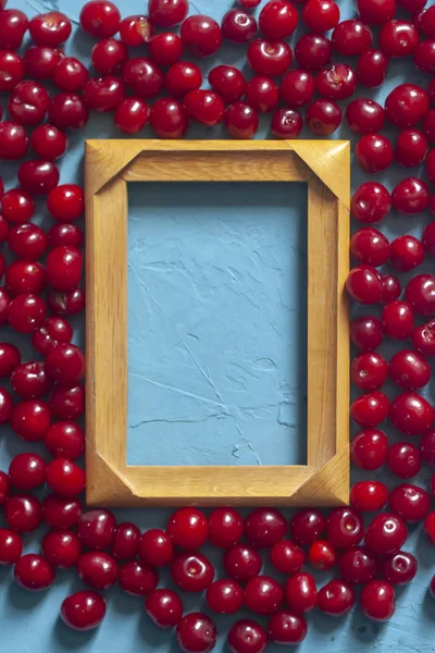 Marco de madera con espacio de copia y cerezas maduras sobre fondo azul. Bayas y frutas alrededor del marco de madera vacío — Foto de stock gratuita