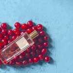 Cerises et bouteille de verre de parfum. Pile de cerises mûres et bouteille en verre de parfum sur fond bleu. Baies biologiques fraîches .