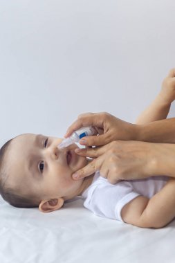 Küçük çocuk burun damlası alıyor. Pediatrist bebek burnuna tuzlu damla koyuyor. Anne elleri bebeğin burnunu temizliyor. 6 aylık çocuk burun damlaları alır.