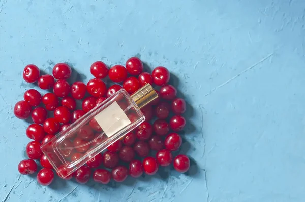 Frasco de vidrio de cerezas y perfume. Montón de cerezas maduras y botella de vidrio de perfume sobre fondo azul. Bayas orgánicas frescas . — Foto de stock gratis