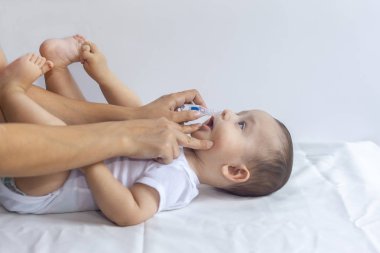 Küçük çocuk burun damlası alıyor. Pediatrist bebek burnuna tuzlu damla koyuyor. Anne elleri bebeğin burnunu temizliyor. 6 aylık çocuk burun damlaları alır.