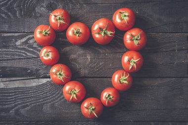 Kalp şekli koyu rustik ahşap arka plan üzerinde taze toplenmiş domates ile oluşan