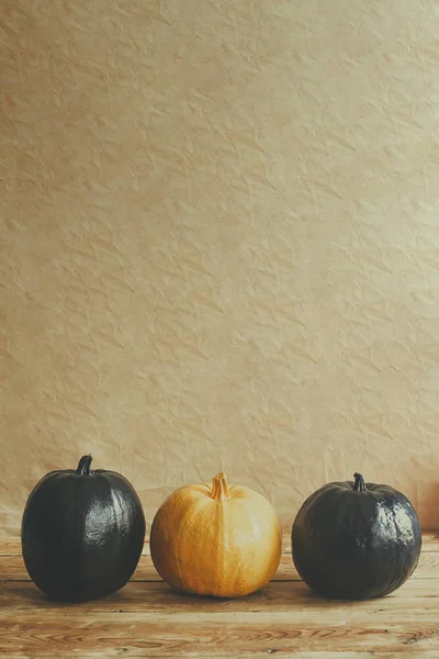 Abóboras de Halloween coloridas na mesa de madeira. Diferença. Sozinho entre os outros. Abóbora laranja única em uma fileira de abóboras pretas — Fotografia de Stock