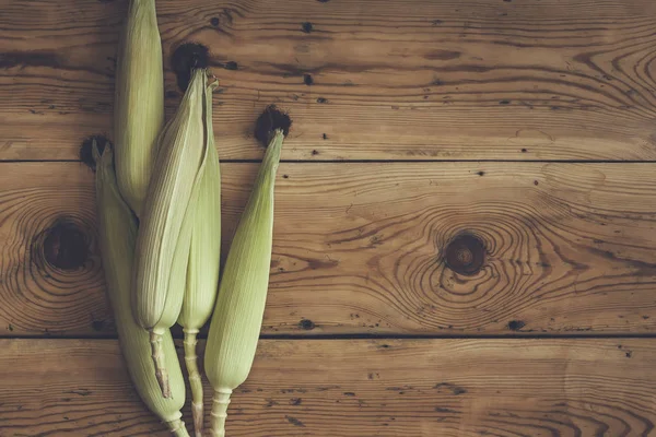 Świeże kolby surowe kukurydzy na drewnianym tle. Kukurydza surowa ze skórą — Zdjęcie stockowe