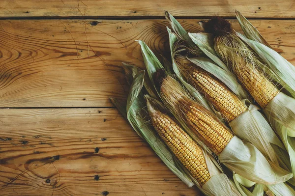 Verse rauwe maïs Cobs op houten achtergrond. Ruwe maïs met huid — Gratis stockfoto