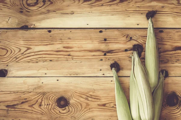 Świeże kolby surowe kukurydzy na drewnianym tle. Kukurydza surowa ze skórą — Zdjęcie stockowe