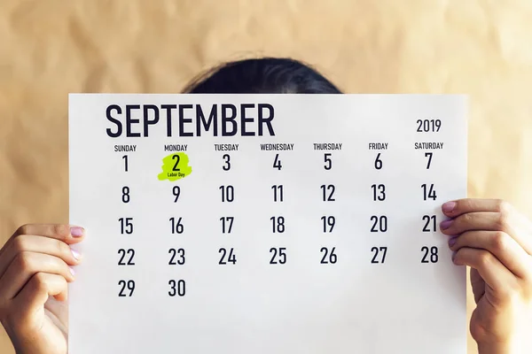 一位妇女拿着八月日历,上面标有劳动节。9月2日,在2019日历上标记 — 图库照片