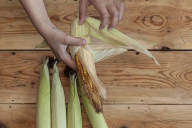 Genç kadın temizlik taze ahşap arka planda koçanı ham Mısır aldı. Shucking Mısır süreci