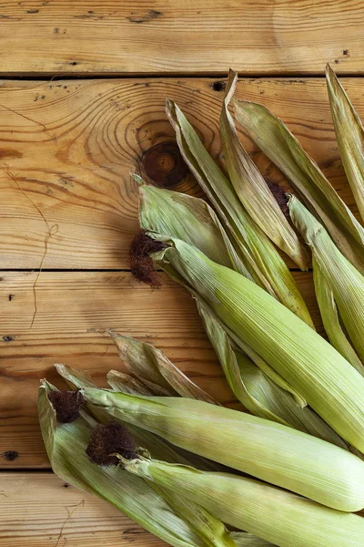 Ahşap arka planda taze ham Mısır koçanı. Deri ile çiğ Mısır