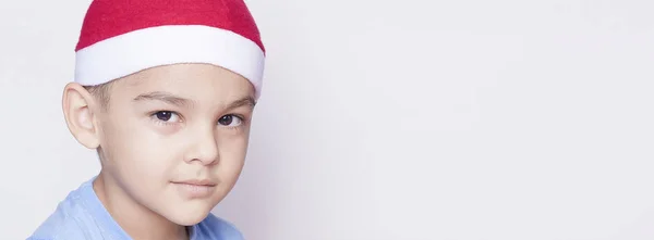 Retrato de un niño de seis años sobre el fondo blanco. Celebrando la Navidad. Niño de 6-7 años con sombrero de Santa . — Foto de Stock