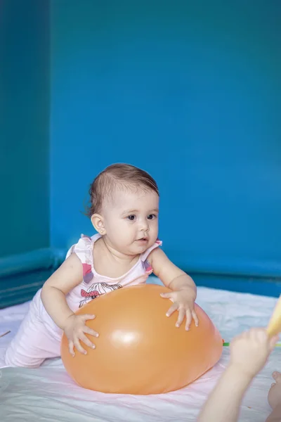 Το μωρό παίζει με ένα μπαλόνι. Το κοριτσάκι να κάνει τις καθημερινές της δραστηριότητες. Μικρό χαριτωμένο κορίτσι μαθαίνοντας να σταθεί και να περπατήσει. — Φωτογραφία Αρχείου