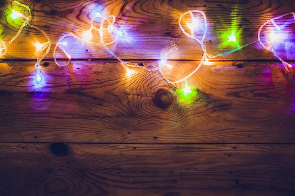 Christmas decorative lights. Christmas garland lights on wood. Colorful Xmas light bulbs on rustic brown plank