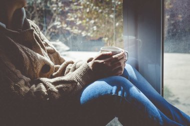 Genç esmer kadın bir fincan çay içiyor. Evde pencerenin yanında oturan kadın. Soğuk sonbahar günleri. Sonbahar arka planı.