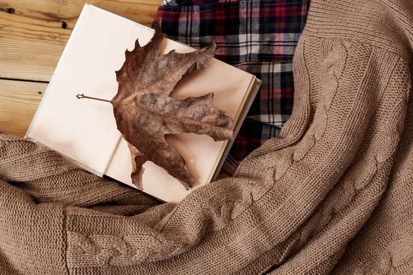 Fall background. Opened book and a big dry fall leaf. Knitted sweater