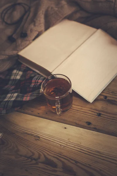 Fondo de caída. Composición otoñal con té caliente, libro, flor de rosa seca y suéter de punto. Una taza de té caliente, bufanda de punto en la mesa de madera . — Foto de Stock