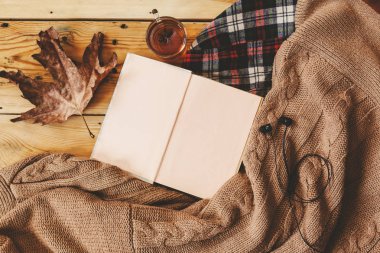 Sonbahar arka plan. Açılan kitap, sonbahar yaprağı ve örme kazak. Bir fincan sıcak çay, tahta masanın üzerine örülmüş atkı. Sonbahar ısınma içecek