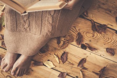 Kitap okuyorum. Kadın sonbahar yaprakları ile ahşap zeminde oturup. Kadın örme ekose ile kaplı ve ilginç kitap okuma
