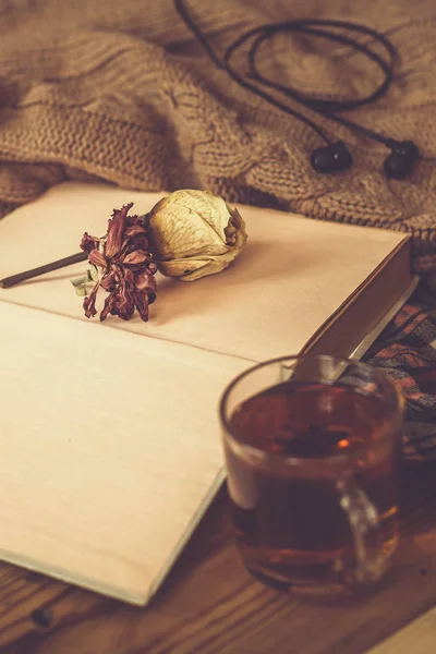 Fall background. Compoziția de toamnă cu ceai fierbinte, carte, floare de trandafir uscată și pulover tricotat. O ceașcă de ceai fierbinte, eșarfă tricotată pe masă de lemn . — Fotografie, imagine de stoc