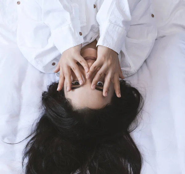 美丽的女人躺在床上。 性感的黑发女士摆着姿势，手指插在嘴里。 女性享受，咬手指。 快乐、娱乐、满足和享受. — 图库照片