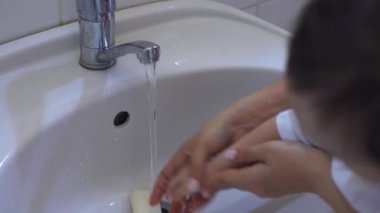 Genç anne yeni yürümeye başlayan bebek ellerini yıkıyor.