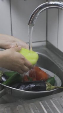 Yeni toplanmış organik sebzeleri süzgeçle yıkayan bir kadın.