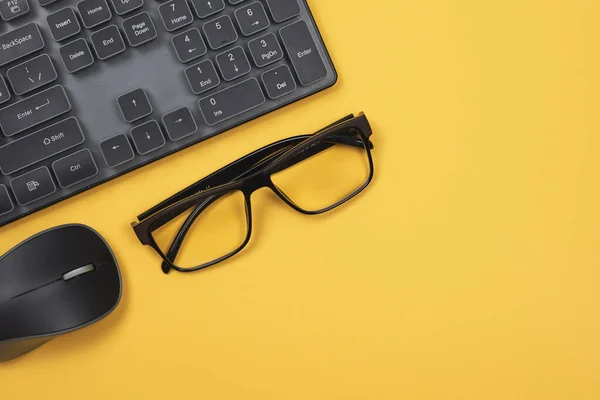 Pc mouse, keyboard and eyeglasses on yellow