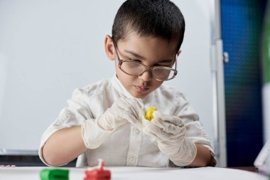 Gözlüklü ve eldivenli bir çocuk plastikle oynuyor.