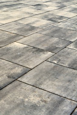Dikdörtgen taş fayanslardan yapılmış çağdaş bir şehir kaldırımının yakın görüntüsü. Gri ve bej renklerin farklı tonları, arka plana doğru çekilen soyut ve dokulu bir desen oluşturur..